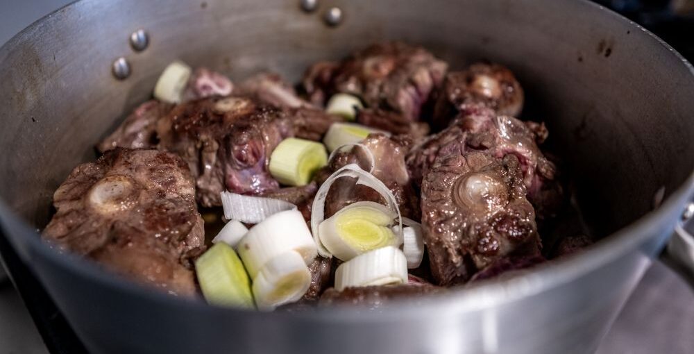 Oxtail and beef bones cooking in a pot with vegetables, showing slow cooking method for flavorful meals