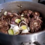 Oxtail and beef bones cooking in a pot with vegetables, showing slow cooking method for flavorful meals