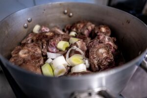 Oxtail and beef bones cooking in a pot with vegetables, showing slow cooking method for flavorful meals