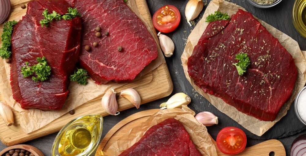 Raw grass-fed beef steaks with herbs and ingredients on a wooden surface for meal preparation