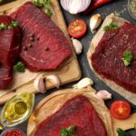Raw grass-fed beef steaks with herbs and ingredients on a wooden surface for meal preparation