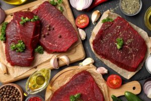 Raw grass-fed beef steaks with herbs and ingredients on a wooden surface for meal preparation