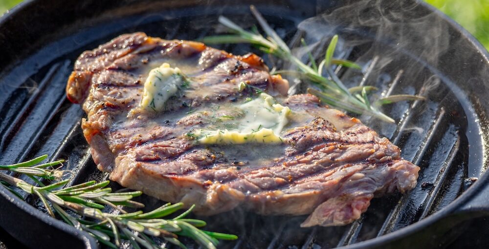 Grass-fed steak searing in a cast iron skillet with butter and herbs for a perfect crust