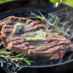 Grass-fed steak searing in a cast iron skillet with butter and herbs for a perfect crust