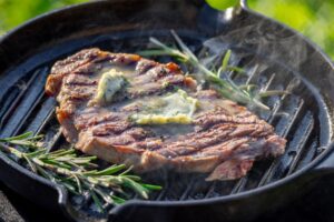 Grass-fed steak searing in a cast iron skillet with butter and herbs for a perfect crust