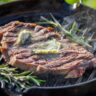 Grass-fed steak searing in a cast iron skillet with butter and herbs for a perfect crust